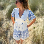 Leichtes kurzes Kleid mit V Ausschnitt und kurzen Flügelärmeln. Das Kleid ist weiß mit blauen Blumenstickereien.