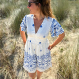 Leichtes kurzes Kleid mit V Ausschnitt und kurzen Flügelärmeln. Das Kleid ist weiß mit blauen Blumenstickereien.