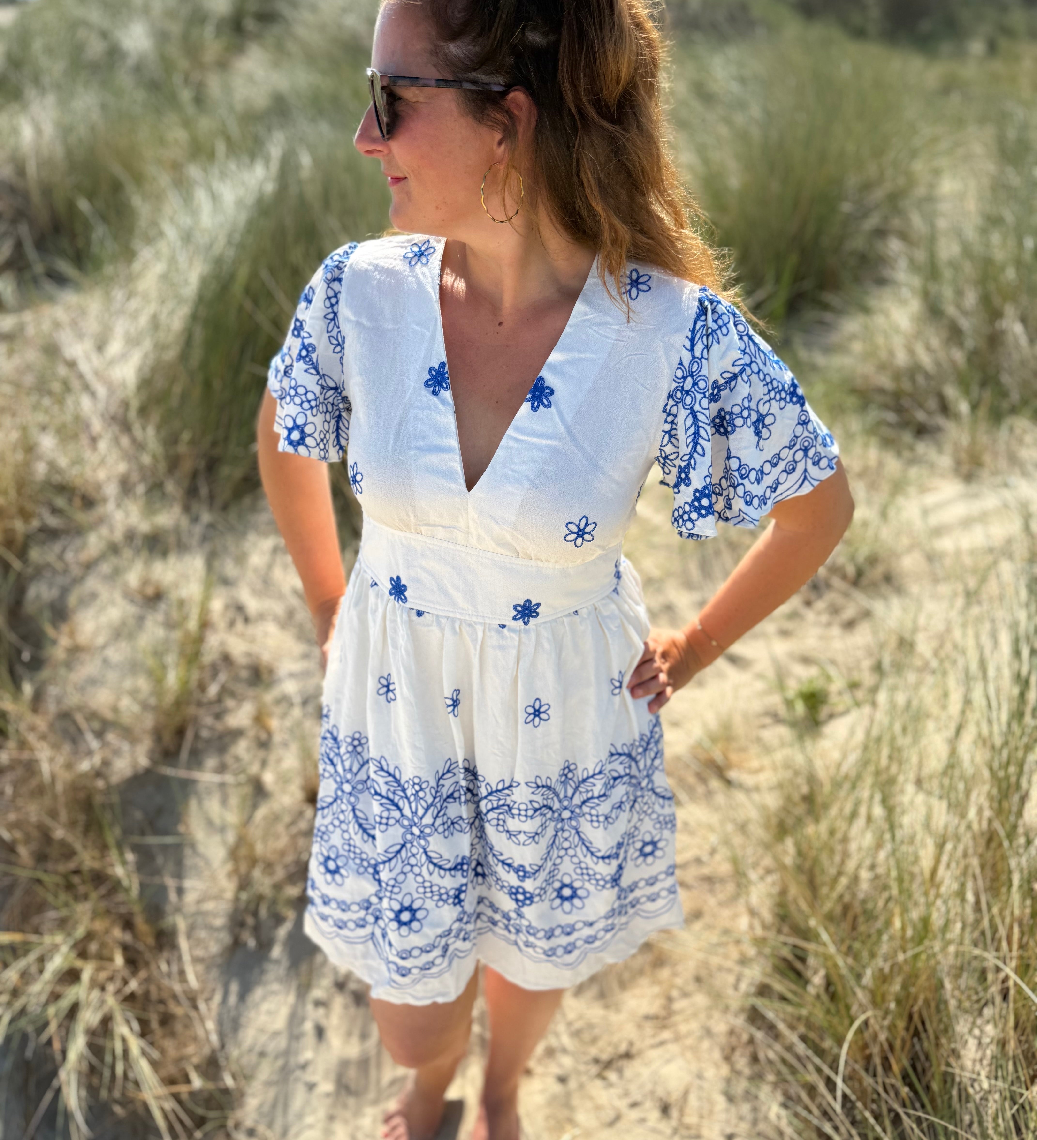 Leichtes kurzes Kleid mit V Ausschnitt und kurzen Flügelärmeln. Das Kleid ist weiß mit blauen Blumenstickereien.