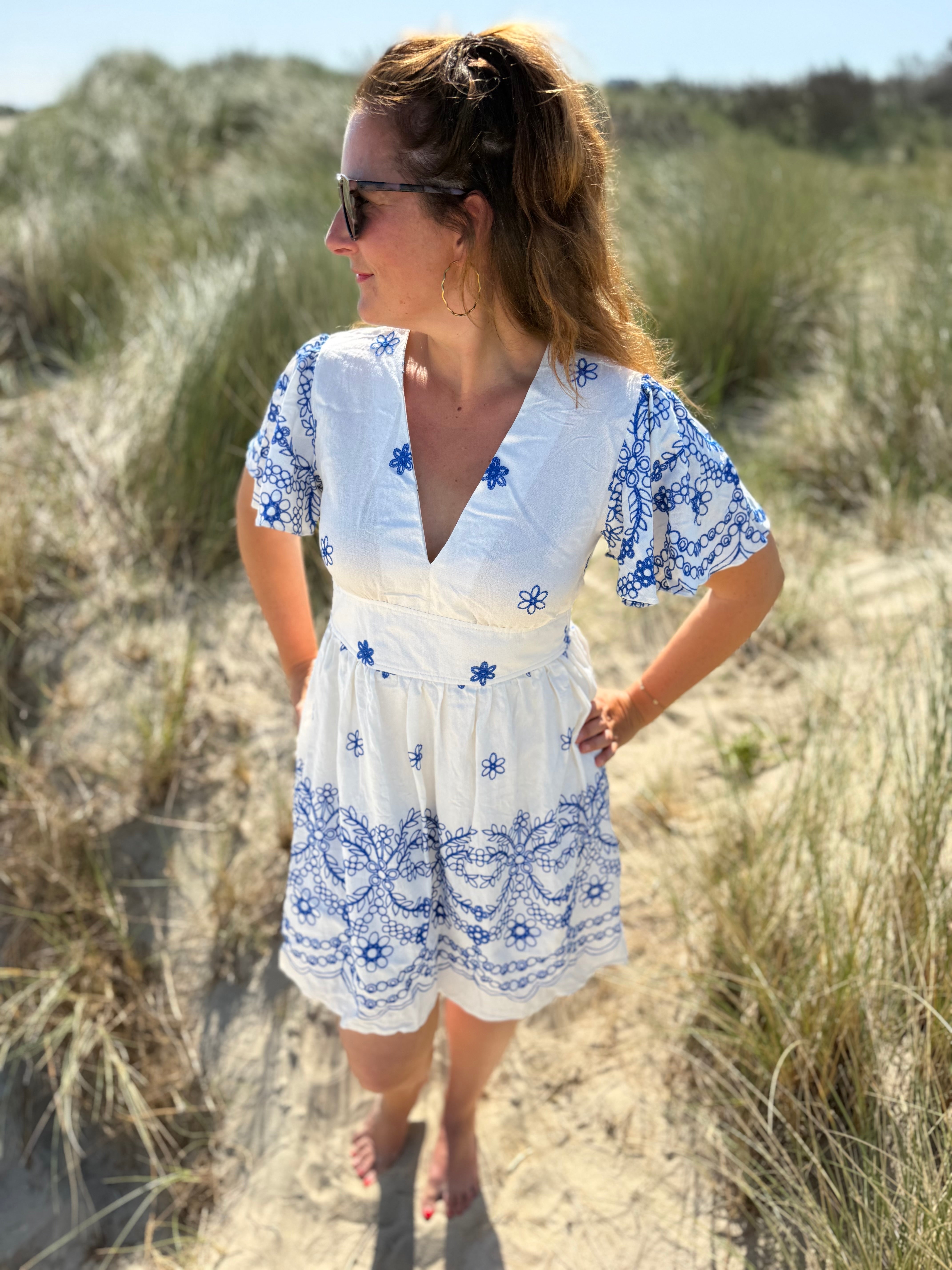 Leichtes kurzes Kleid mit V Ausschnitt und kurzen Flügelärmeln. Das Kleid ist weiß mit blauen Blumenstickereien.