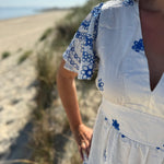 Leichtes kurzes Kleid mit V Ausschnitt und kurzen Flügelärmeln. Das Kleid ist weiß mit blauen Blumenstickereien.