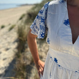 Leichtes kurzes Kleid mit V Ausschnitt und kurzen Flügelärmeln. Das Kleid ist weiß mit blauen Blumenstickereien.