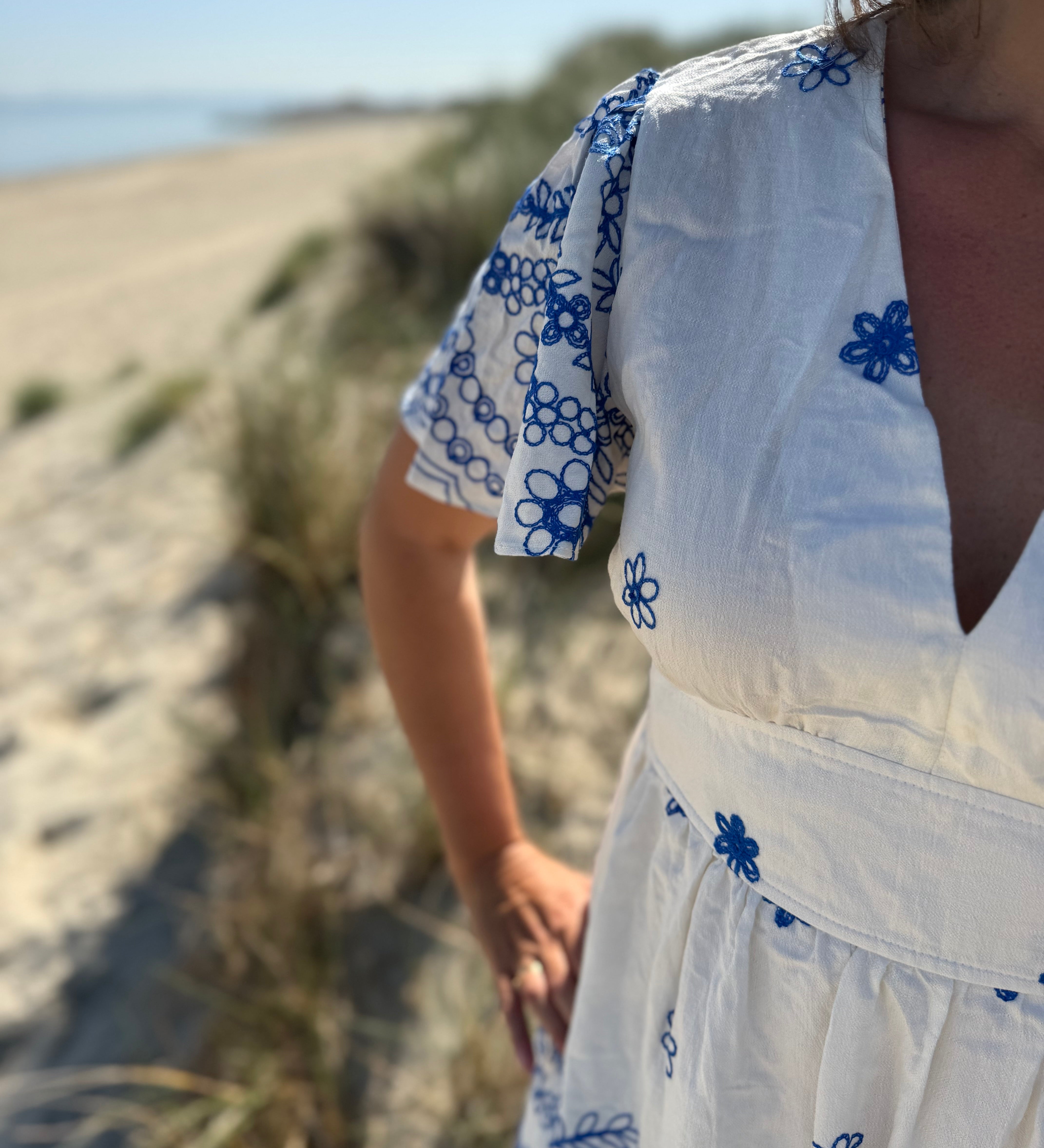 Leichtes kurzes Kleid mit V Ausschnitt und kurzen Flügelärmeln. Das Kleid ist weiß mit blauen Blumenstickereien.