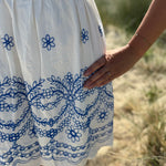 Leichtes kurzes Kleid mit V Ausschnitt und kurzen Flügelärmeln. Das Kleid ist weiß mit blauen Blumenstickereien.