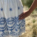 Leichtes kurzes Kleid mit V Ausschnitt und kurzen Flügelärmeln. Das Kleid ist weiß mit blauen Blumenstickereien.