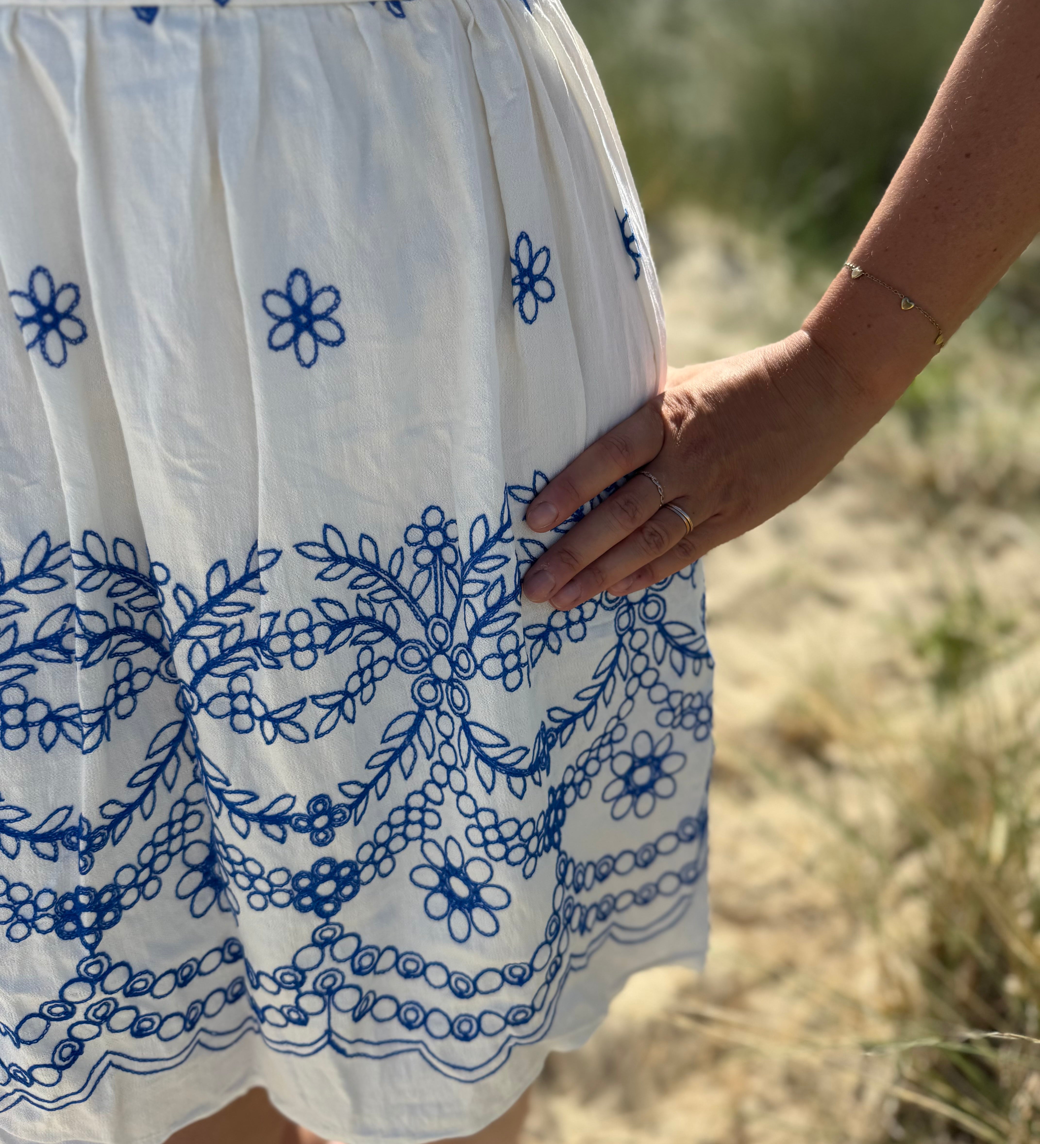 Leichtes kurzes Kleid mit V Ausschnitt und kurzen Flügelärmeln. Das Kleid ist weiß mit blauen Blumenstickereien.
