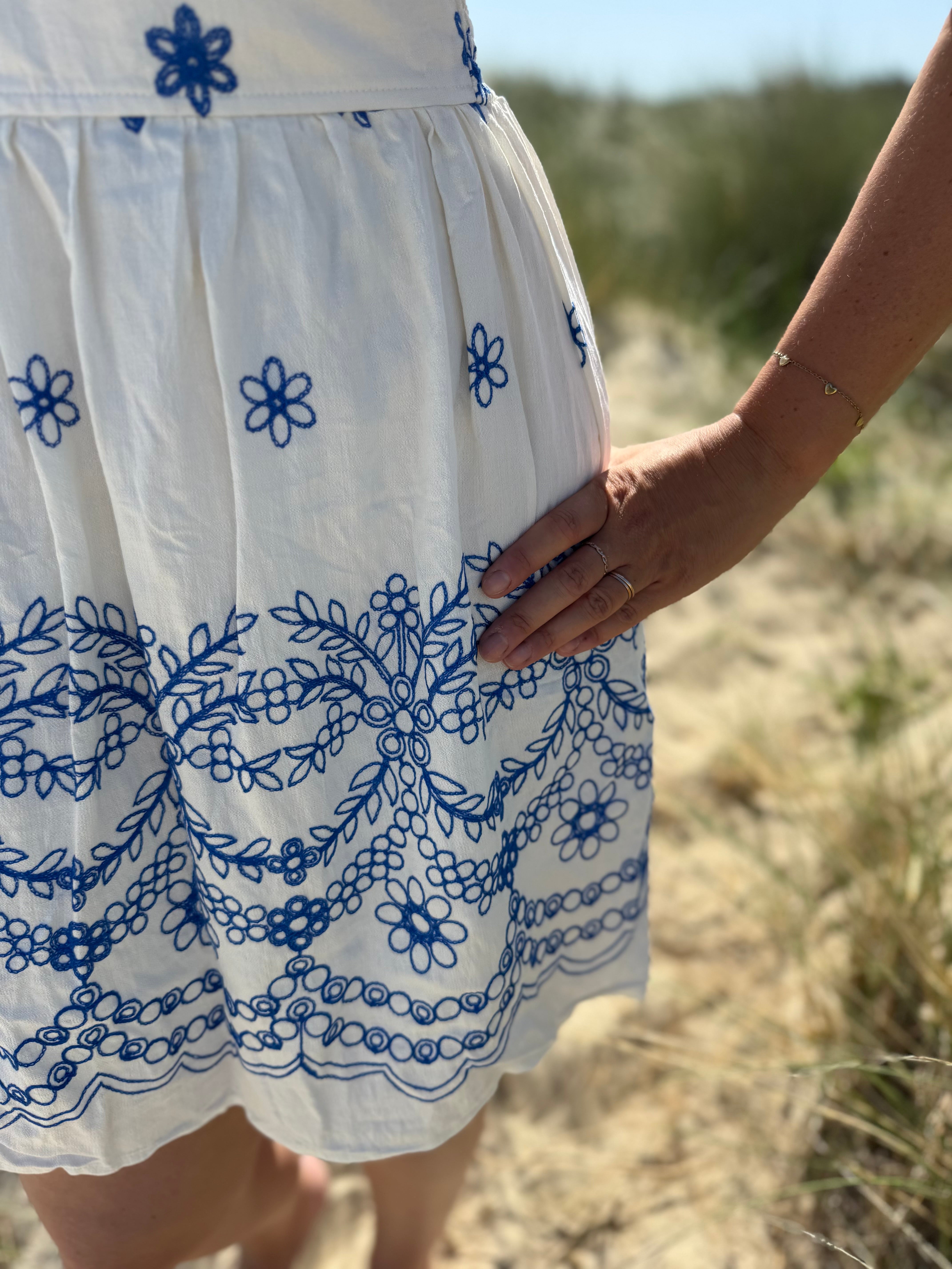 Leichtes kurzes Kleid mit V Ausschnitt und kurzen Flügelärmeln. Das Kleid ist weiß mit blauen Blumenstickereien.