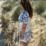Leichtes kurzes Kleid mit V Ausschnitt und kurzen Flügelärmeln. Das Kleid ist weiß mit blauen Blumenstickereien.