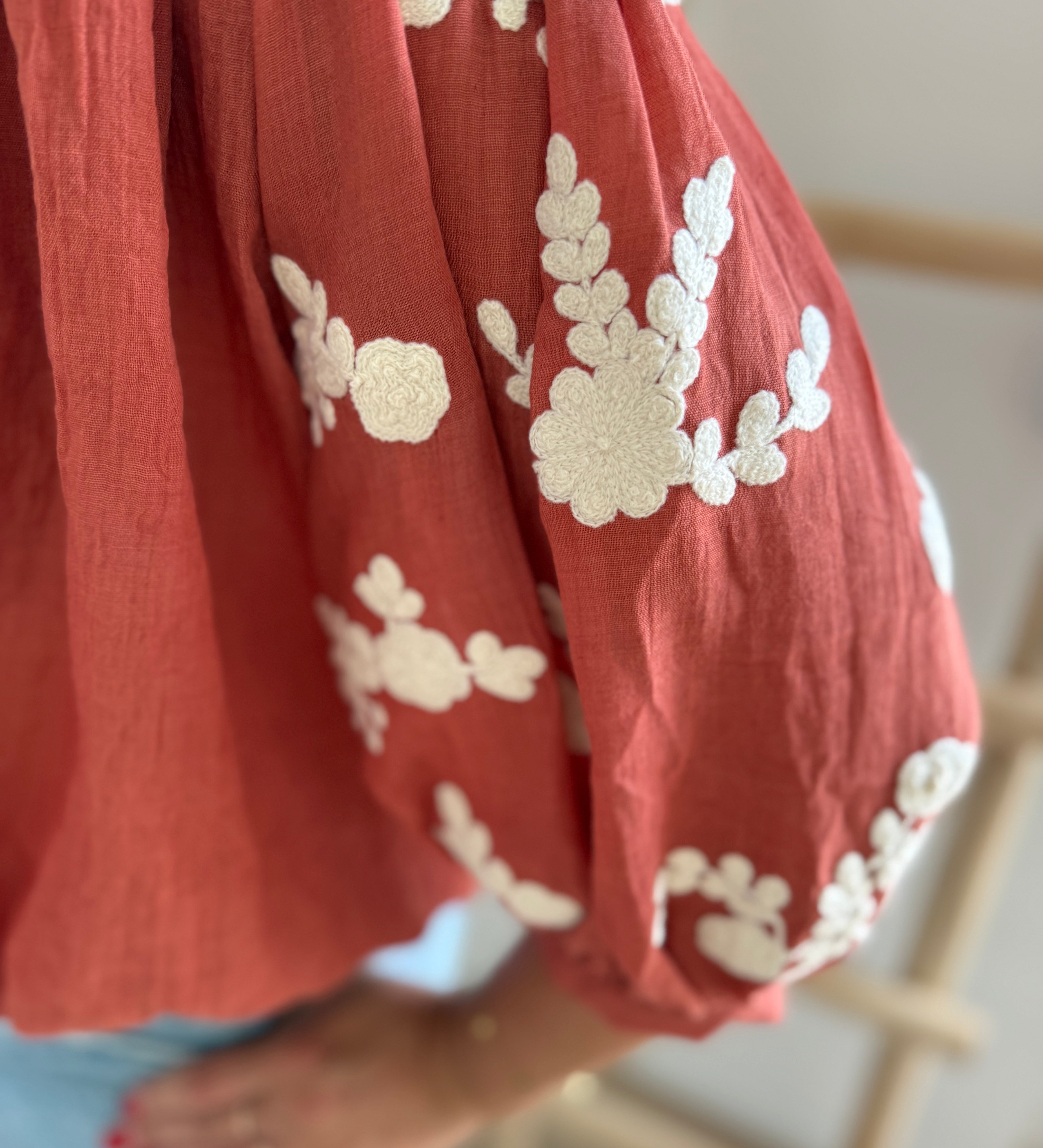 Leichte locker sitzende Baumwollbluse in rostrot mit beigen Blumenstickereien an den Ärmeln.