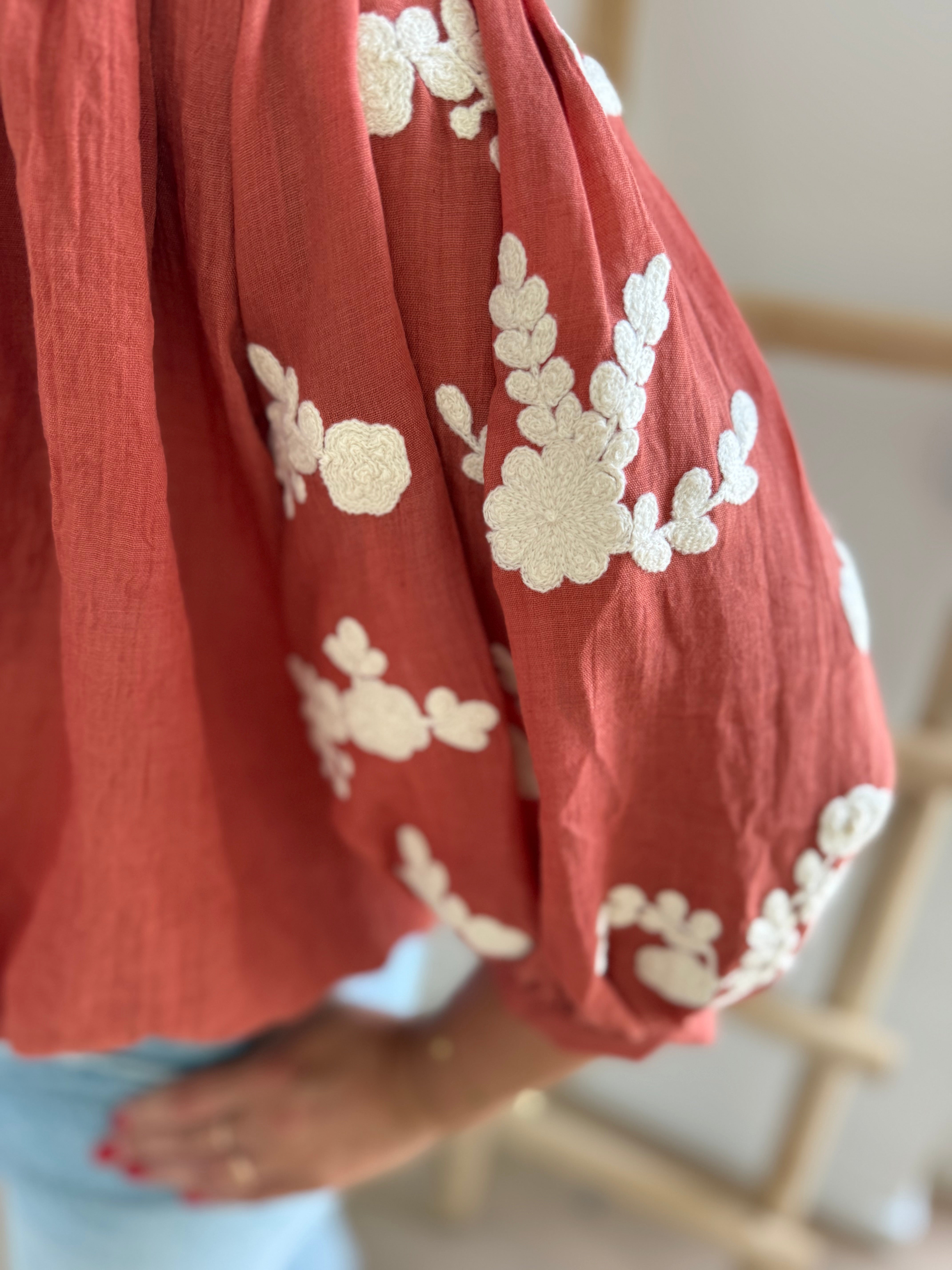 Leichte locker sitzende Baumwollbluse in rostrot mit beigen Blumenstickereien an den Ärmeln.