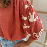 Leichte locker sitzende Baumwollbluse in rostrot mit beigen Blumenstickereien an den Ärmeln.