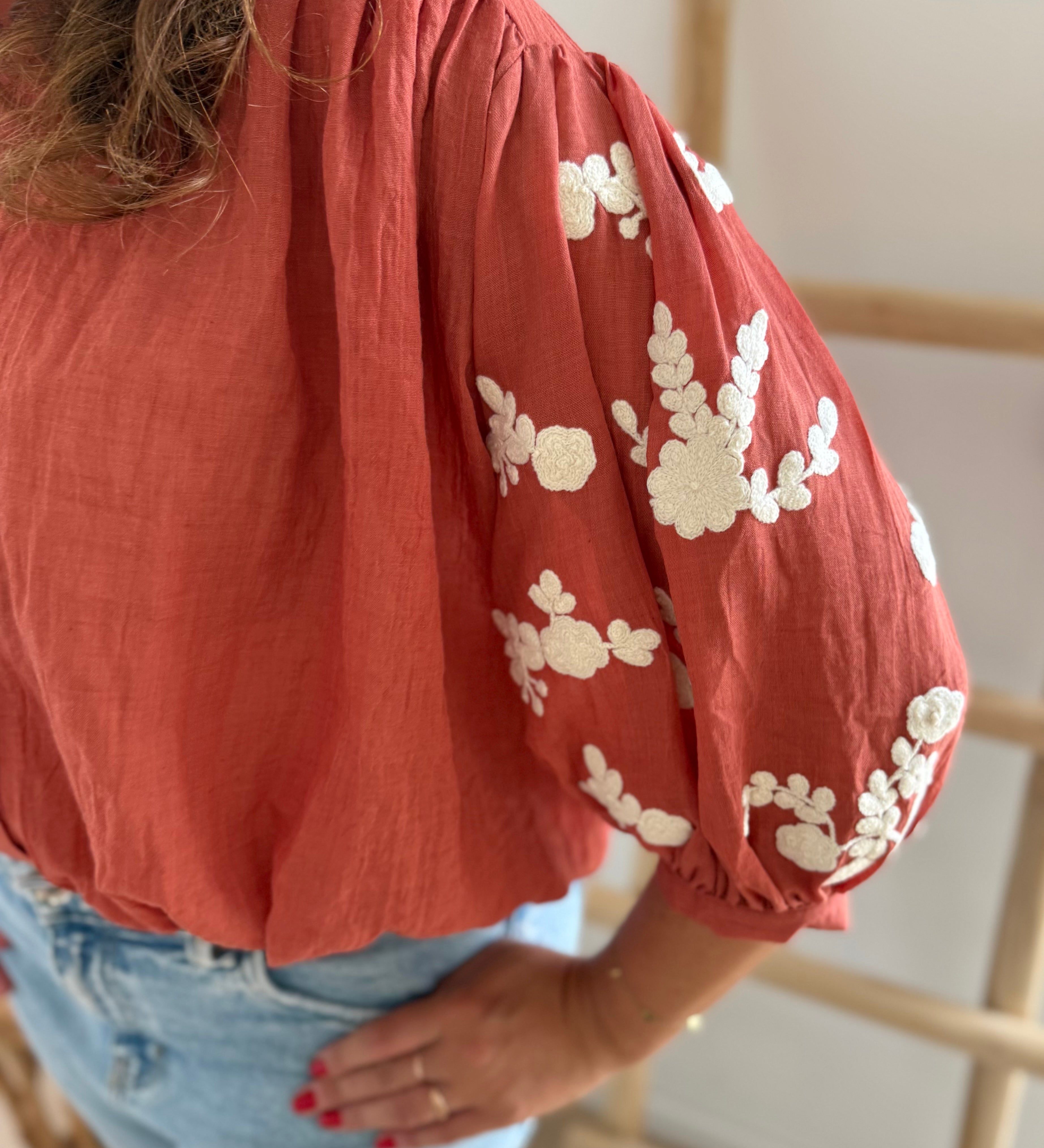 Leichte locker sitzende Baumwollbluse in rostrot mit beigen Blumenstickereien an den Ärmeln.