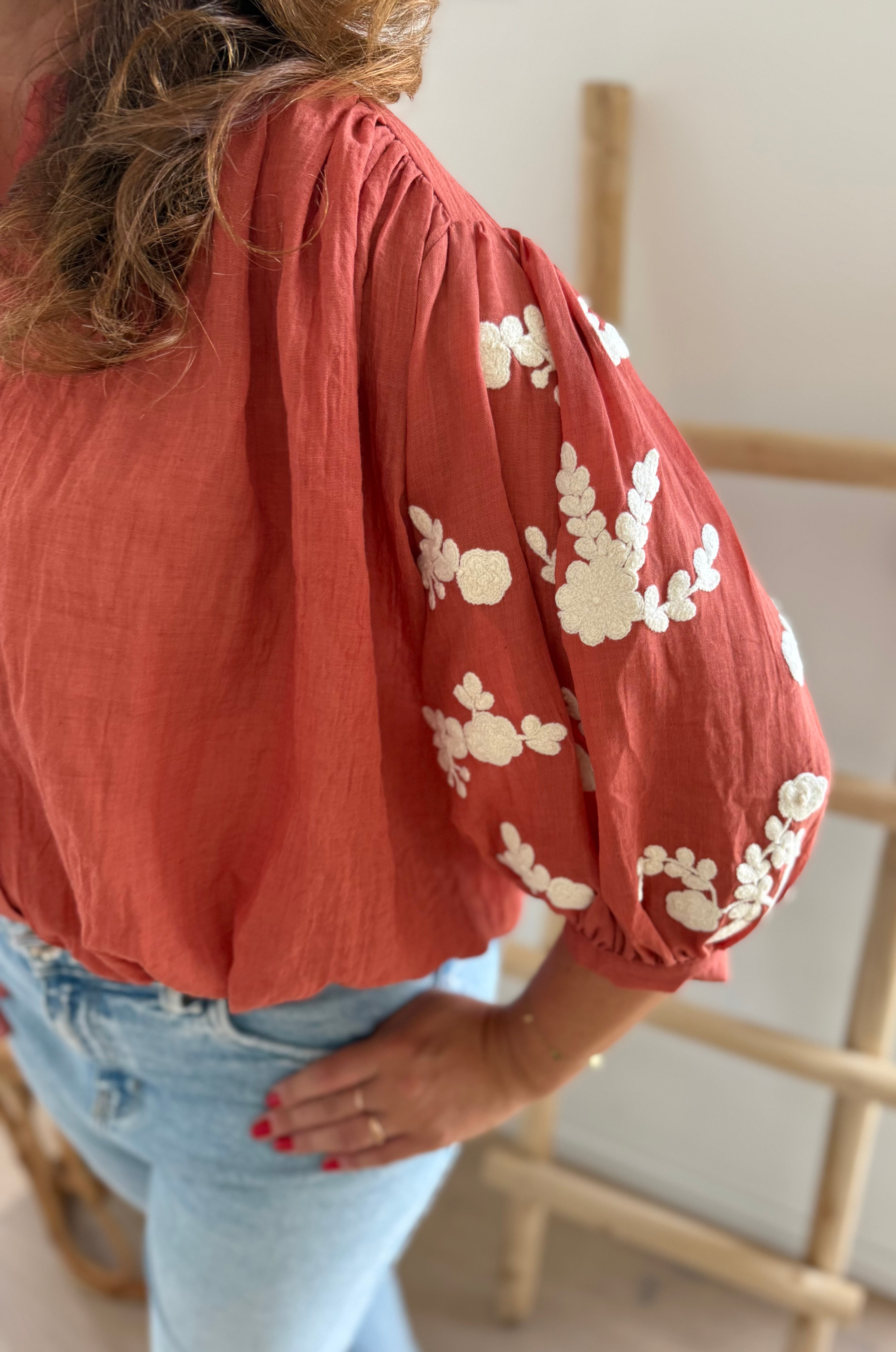 Leichte locker sitzende Baumwollbluse in rostrot mit beigen Blumenstickereien an den Ärmeln.