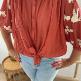 Leichte locker sitzende Baumwollbluse in rostrot mit beigen Blumenstickereien an den Ärmeln.