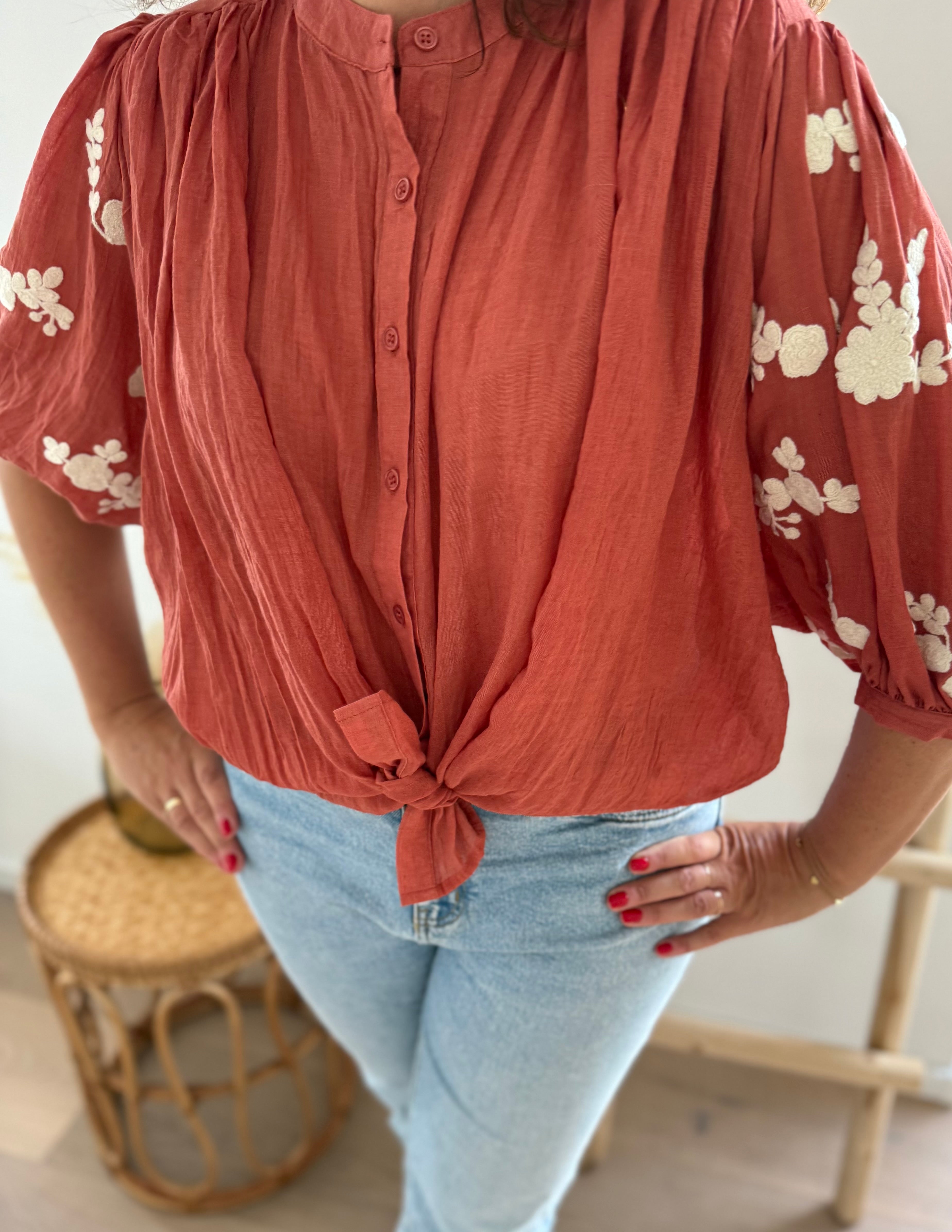 Leichte locker sitzende Baumwollbluse in rostrot mit beigen Blumenstickereien an den Ärmeln.