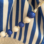 Gestreifte Tasche mit Bast am unteren Teil und einer abnehmbaren Perlenkette in den passenden Farben zu den Streifen. Farbe blau beige.