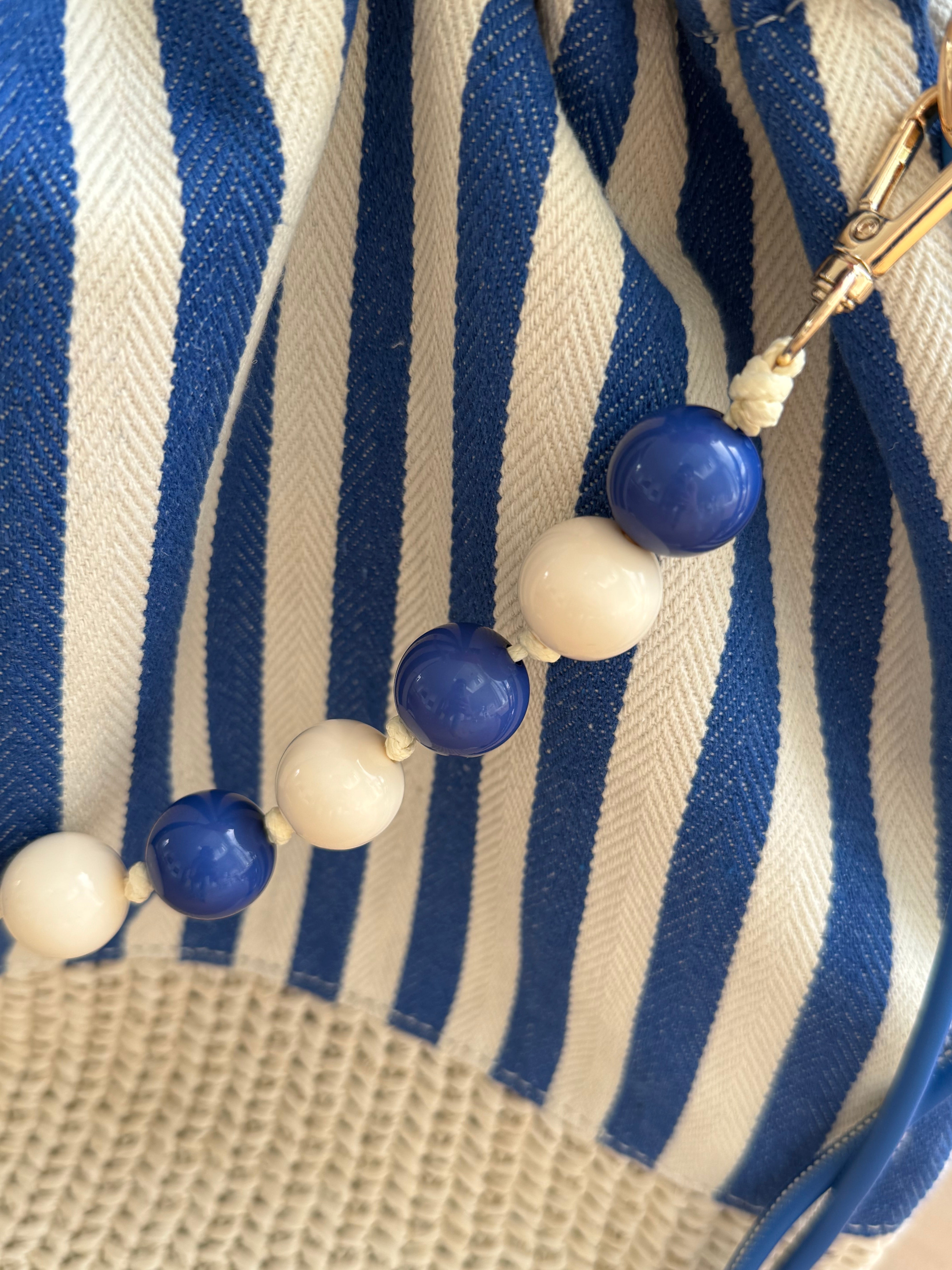 Gestreifte Tasche mit Bast am unteren Teil und einer abnehmbaren Perlenkette in den passenden Farben zu den Streifen. Farbe blau beige.