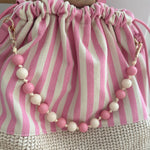 Gestreifte Tasche mit Bast am unteren Teil und einer abnehmbaren Perlenkette in den passenden Farben zu den Streifen. Farbe rosa beige.