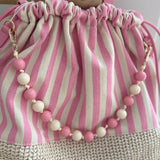 Gestreifte Tasche mit Bast am unteren Teil und einer abnehmbaren Perlenkette in den passenden Farben zu den Streifen. Farbe rosa beige.