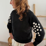 Schwarzer Strickpullover mit verspielten Blumenstickereien auf den Ärmeln in hellbeige.