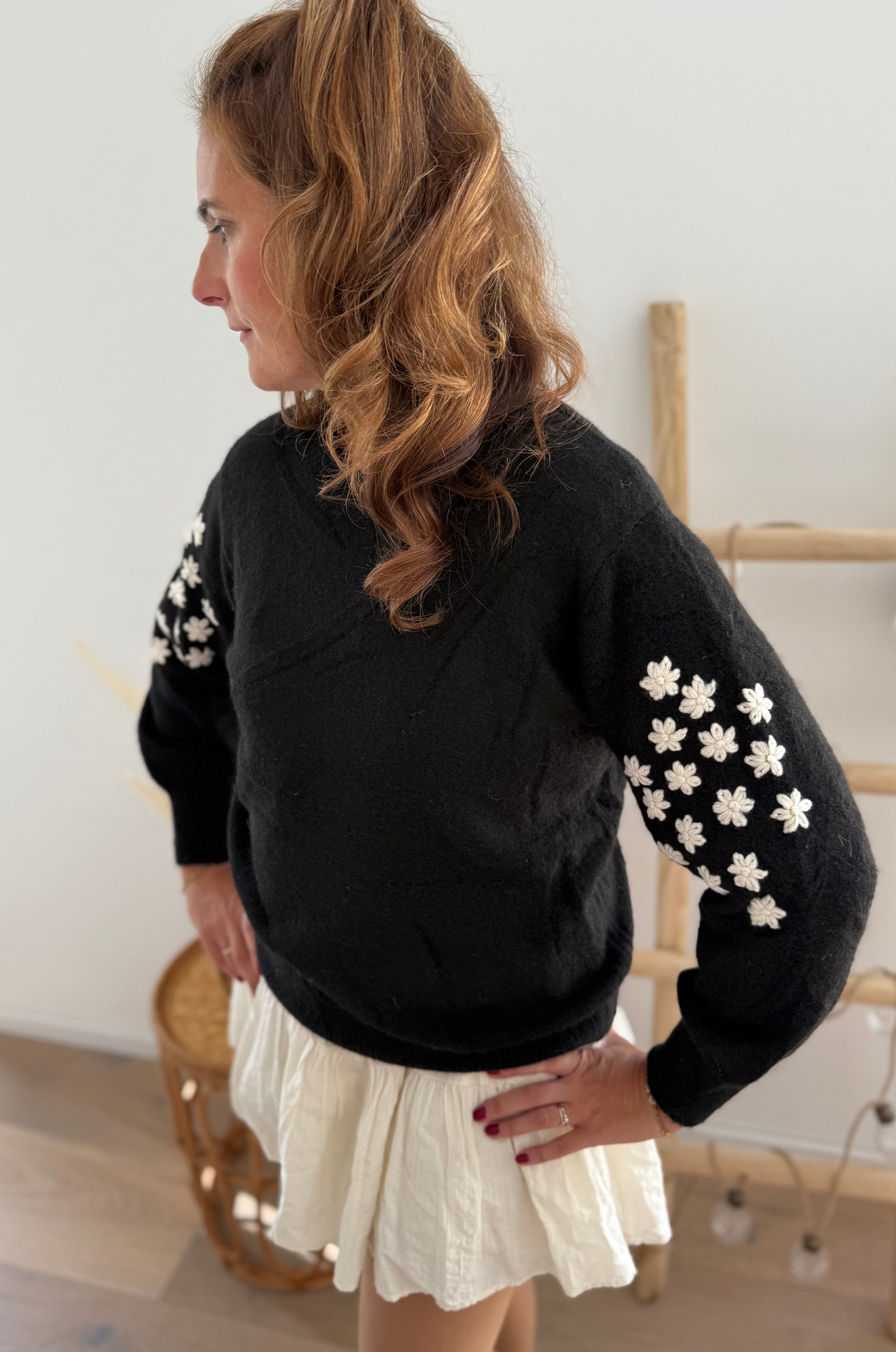 Schwarzer Strickpullover mit verspielten Blumenstickereien auf den Ärmeln in hellbeige.