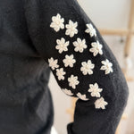 Schwarzer Strickpullover mit verspielten Blumenstickereien auf den Ärmeln in hellbeige.