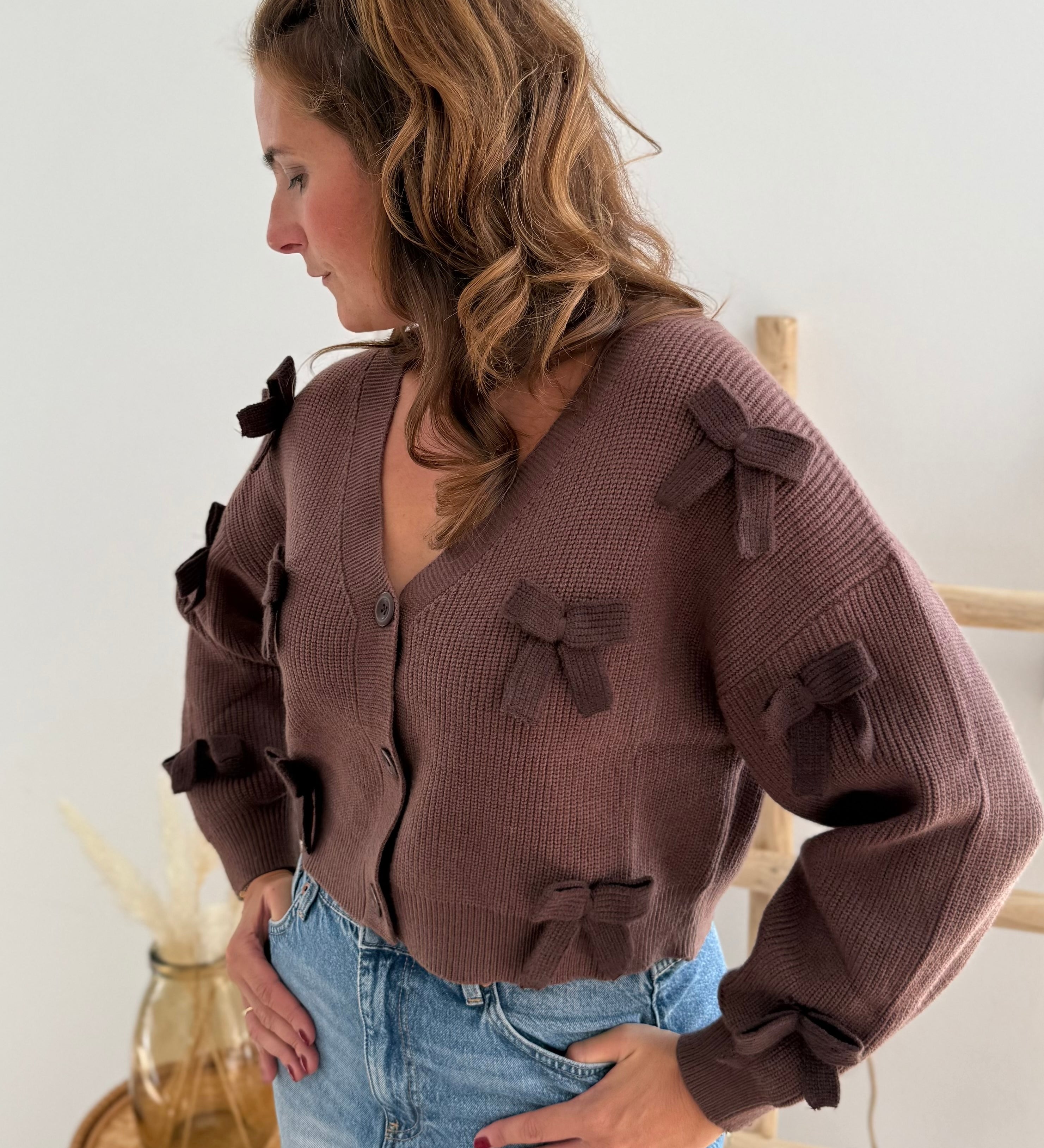 Braune Strickjacke mit V Aussschnitt und einem kurzen Cropped Schnitt. Die Strickjacke ist mit braunen Strickschleifen bestickt.