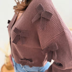 Braune Strickjacke mit V Aussschnitt und einem kurzen Cropped Schnitt. Die Strickjacke ist mit braunen Strickschleifen bestickt.