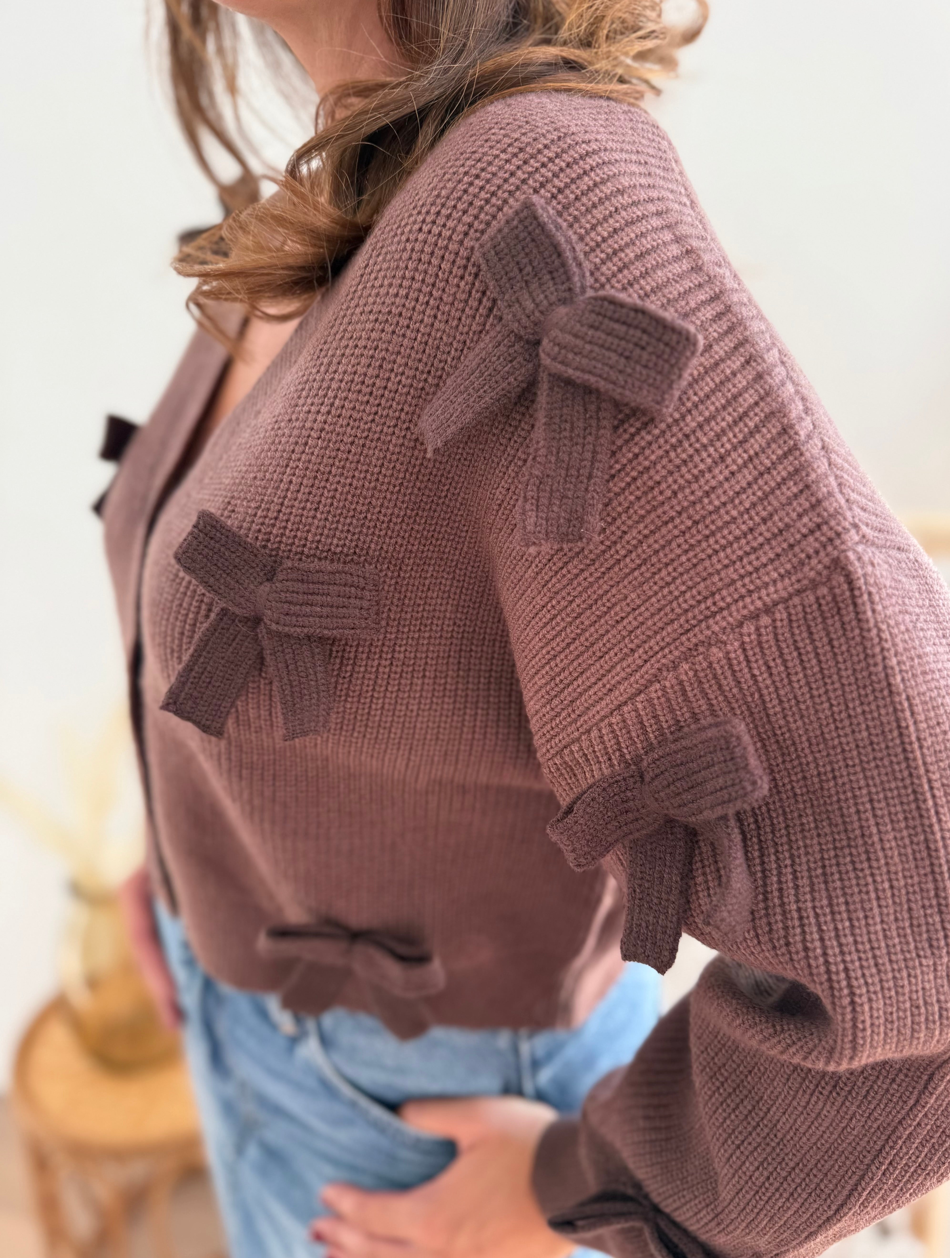 Braune Strickjacke mit V Aussschnitt und einem kurzen Cropped Schnitt. Die Strickjacke ist mit braunen Strickschleifen bestickt.