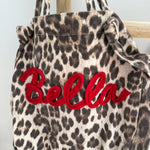 Große Shopper Bag aus strapazierfähigem Denim Stoff. Tasche ist in Leomuster mit rotem "Bella" Schriftzug aufgedruckt.