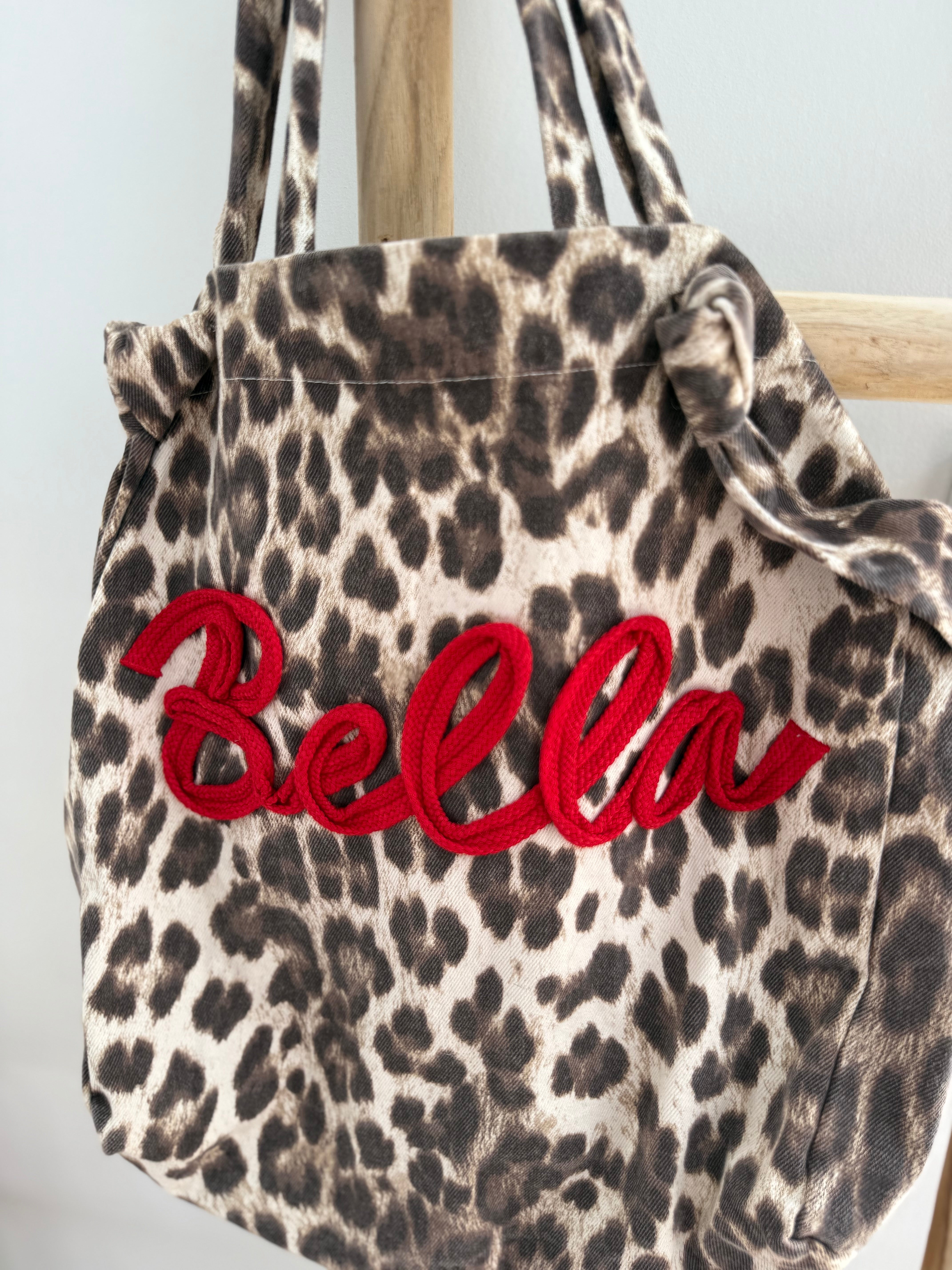 Große Shopper Bag aus strapazierfähigem Denim Stoff. Tasche ist in Leomuster mit rotem "Bella" Schriftzug aufgedruckt.