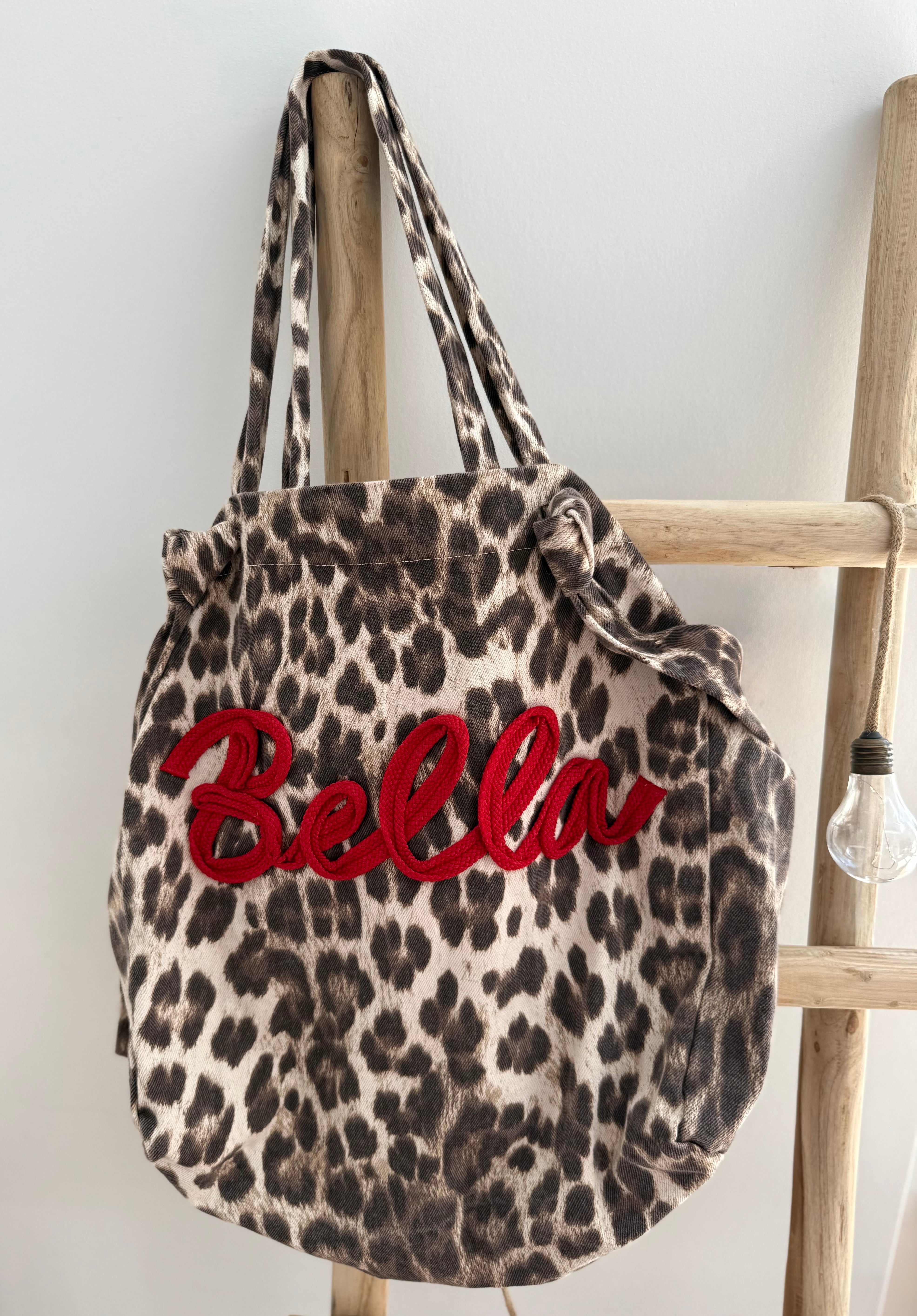 Große Shopper Bag aus strapazierfähigem Denim Stoff. Tasche ist in Leomuster mit rotem "Bella" Schriftzug aufgedruckt.