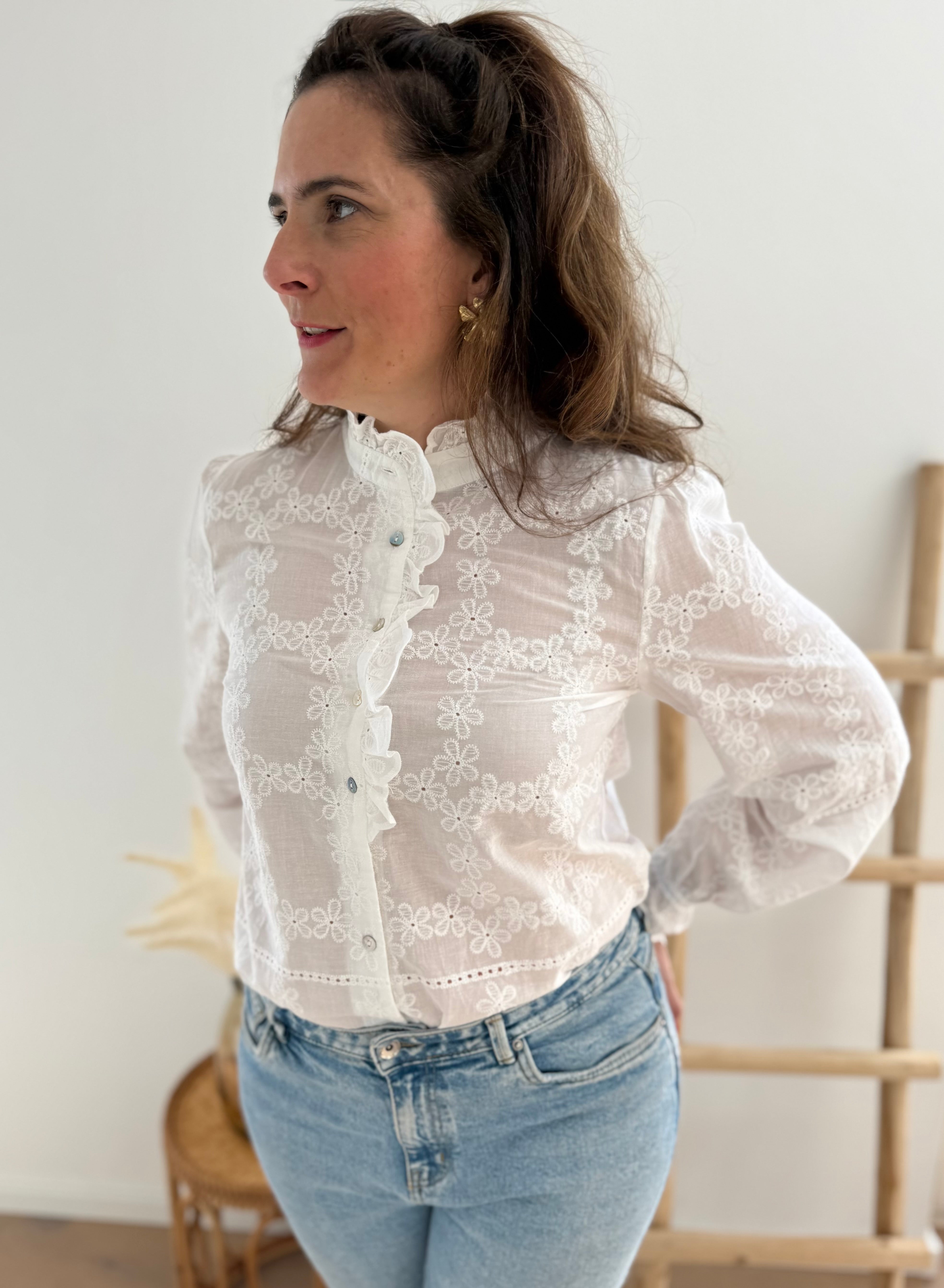 Weiße Bluse mit Blumen Stickereien. Die Bluse hat lange Ärmel, einen verspielter Stehkragen und eine Knopfleiste mit Spitze.