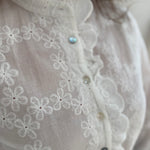 Weiße Bluse mit Blumen Stickereien. Die Bluse hat lange Ärmel, einen verspielter Stehkragen und eine Knopfleiste mit Spitze.