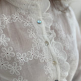 Weiße Bluse mit Blumen Stickereien. Die Bluse hat lange Ärmel, einen verspielter Stehkragen und eine Knopfleiste mit Spitze.