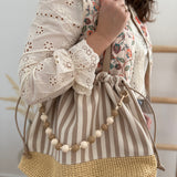 Gestreifte Tasche mit Bast am unteren Teil und einer abnehmbaren Perlenkette in den passenden Farben zu den Streifen. Farbe beige natur