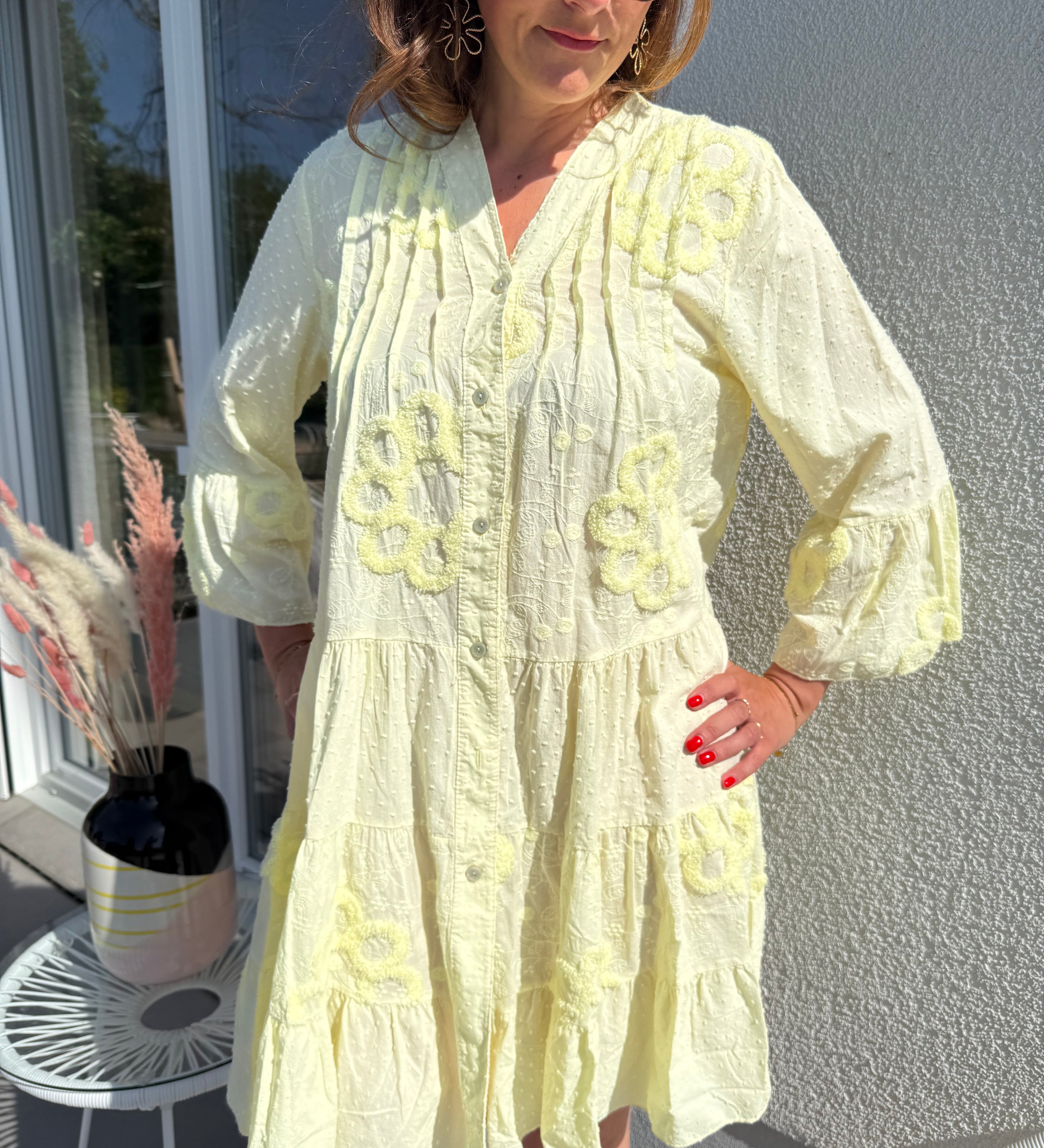 Luftiges kurzes Sommerkleid mit verspielter Blumen Beflockung. Das Kleid fällt locker leicht. Das Kleid hat eine Knopfleiste und einen V Ausschnitt. Die Ärmel sind 3/4 lang. Farbe hellgelb.