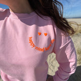Locker geschnittenes Sweatshirt in rosa mit einem orangenen Smiley auf der Brust.