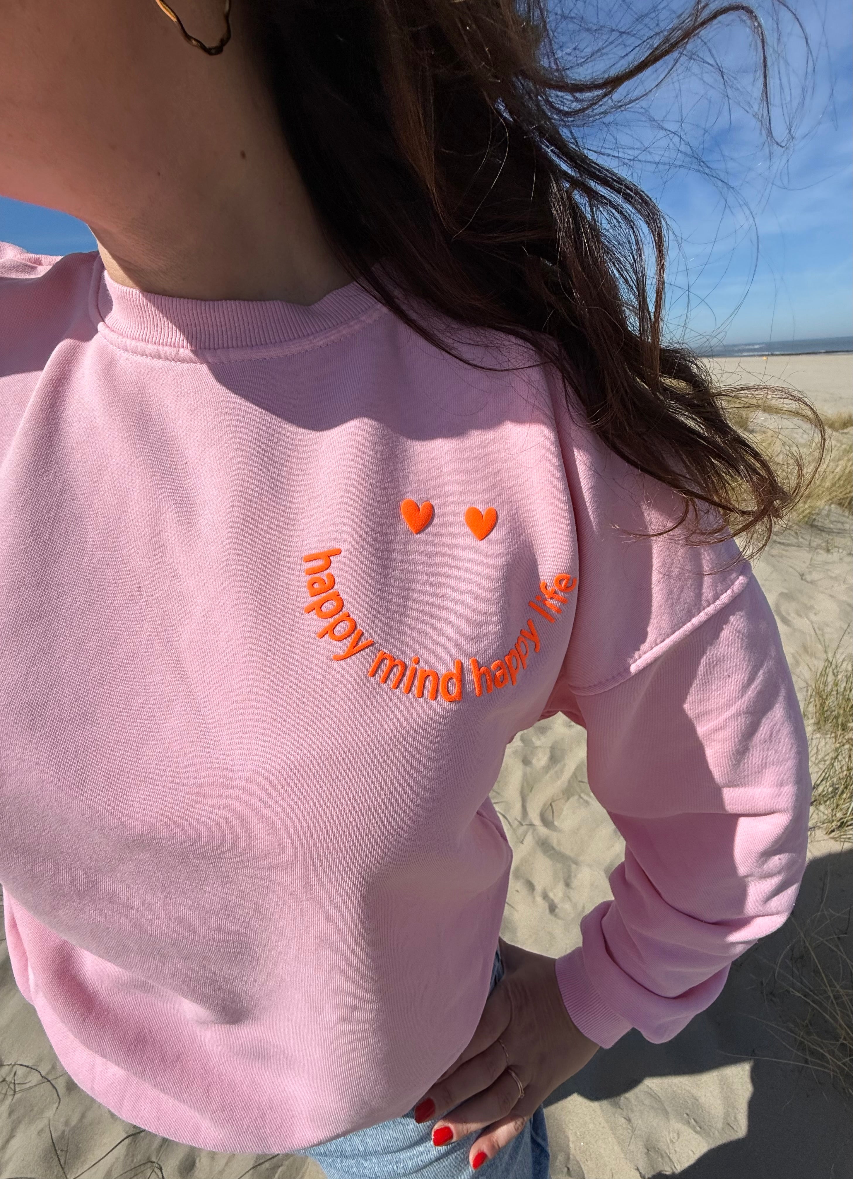 Locker geschnittenes Sweatshirt in rosa mit einem orangenen Smiley auf der Brust.