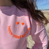 Locker geschnittenes Sweatshirt in rosa mit einem orangenen Smiley auf der Brust.