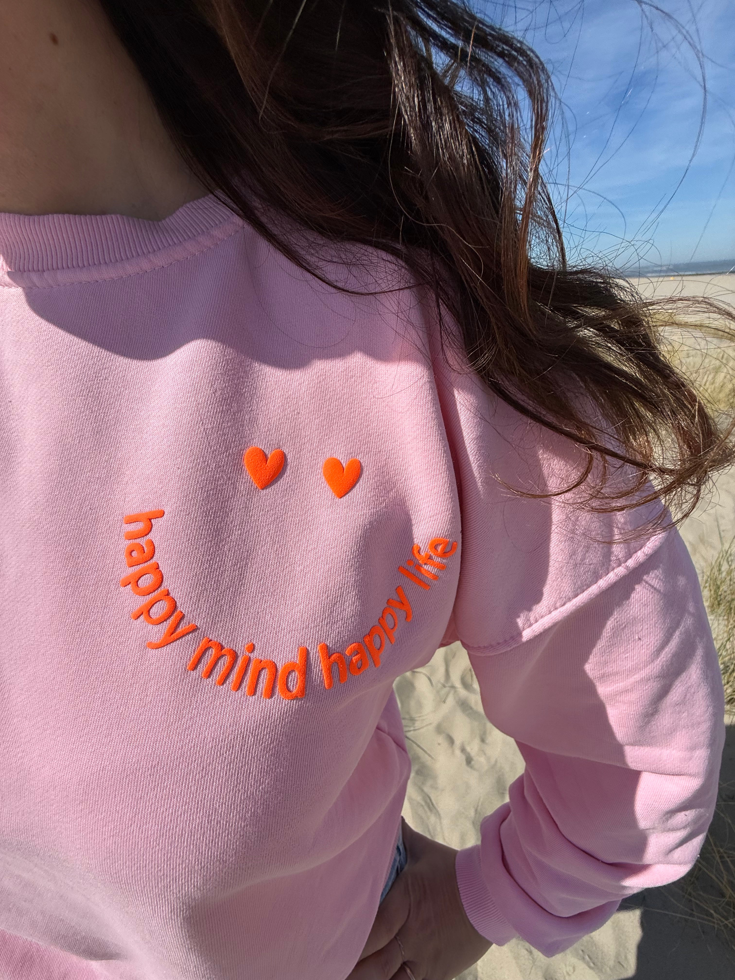 Locker geschnittenes Sweatshirt in rosa mit einem orangenen Smiley auf der Brust.