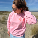 Locker geschnittenes Sweatshirt in rosa mit einem orangenen Smiley auf der Brust.