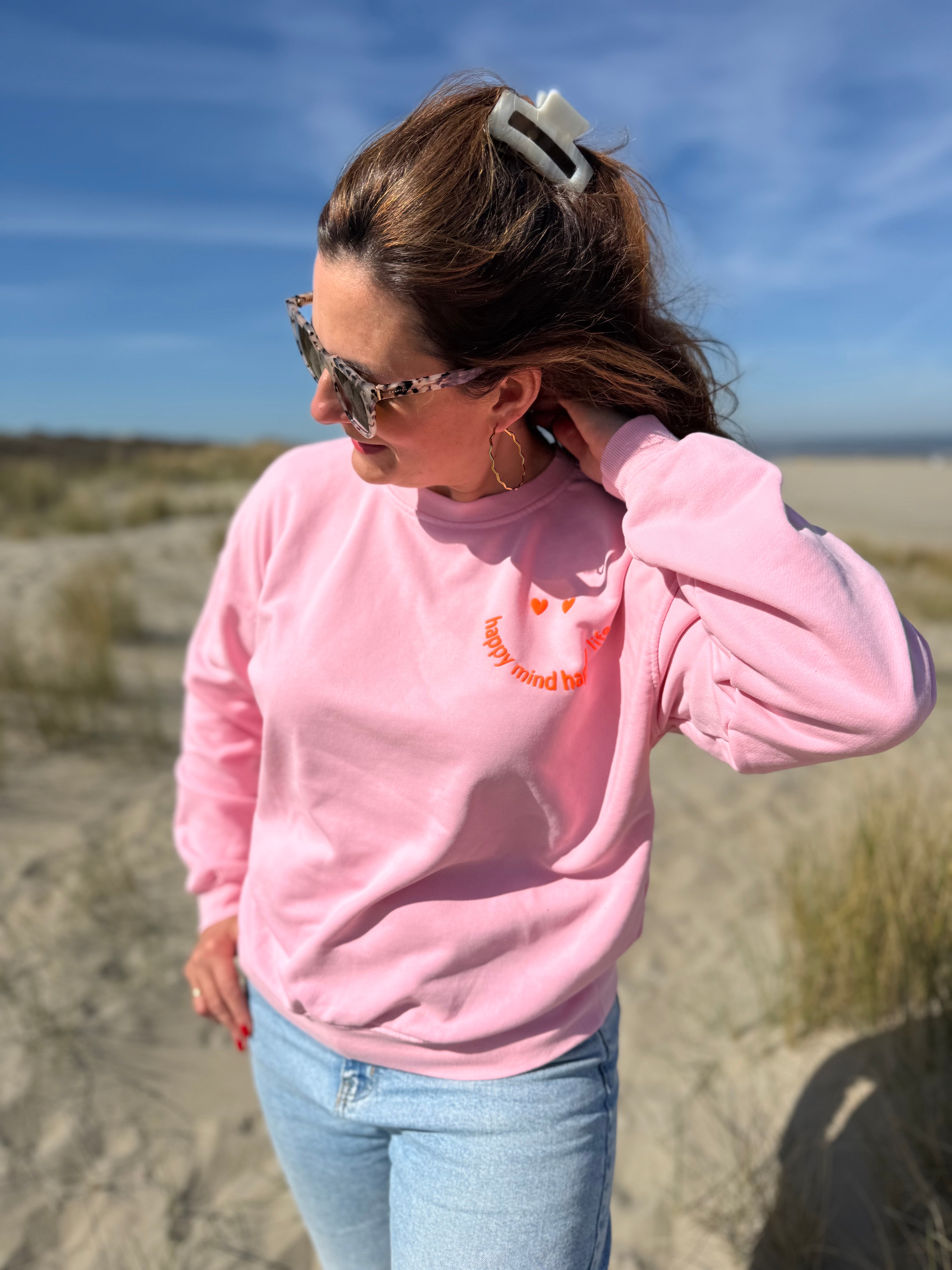 Locker geschnittenes Sweatshirt in rosa mit einem orangenen Smiley auf der Brust.