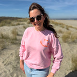 Locker geschnittenes Sweatshirt in rosa mit einem orangenen Smiley auf der Brust.