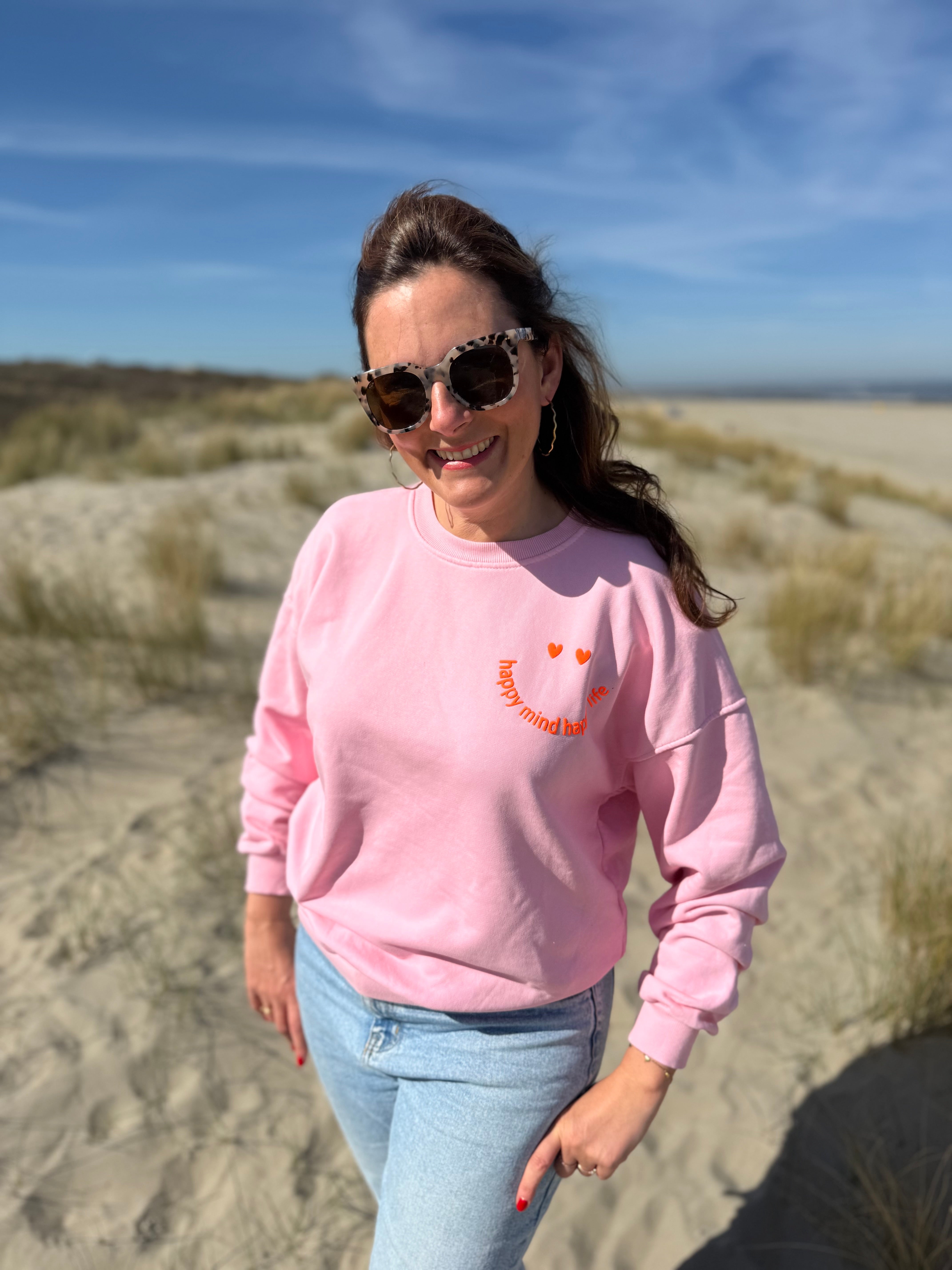 Locker geschnittenes Sweatshirt in rosa mit einem orangenen Smiley auf der Brust.