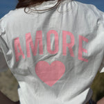 Oversize T-Shirt zum Verlieben. Kleines süßes Herz auf der Brust und ein großer Statement Print auf dem Rücken in rosa mit Amore. Das T-Shirt ist weiß.