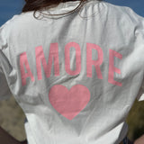 Oversize T-Shirt zum Verlieben. Kleines süßes Herz auf der Brust und ein großer Statement Print auf dem Rücken in rosa mit Amore. Das T-Shirt ist weiß.