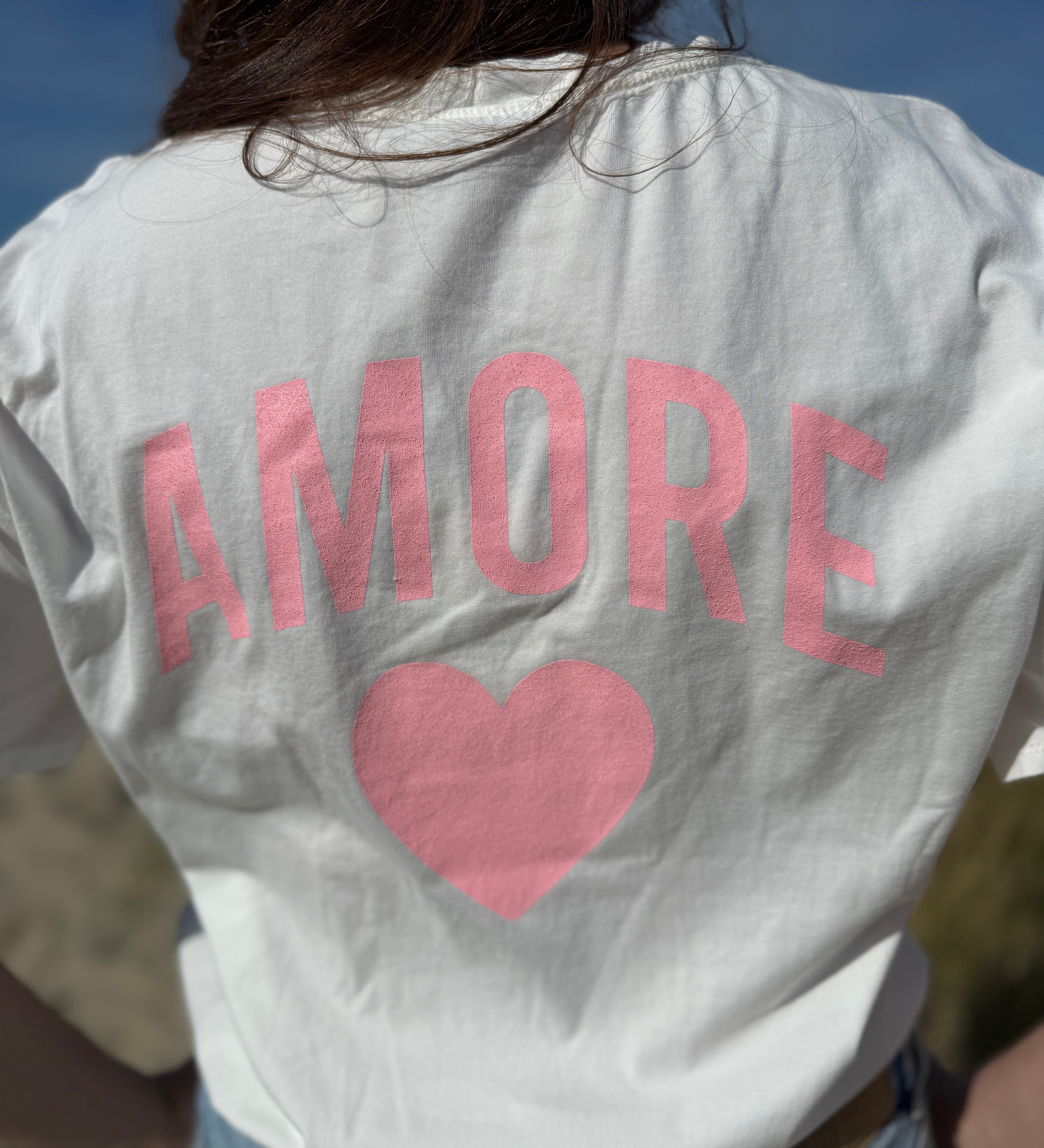Oversize T-Shirt zum Verlieben. Kleines süßes Herz auf der Brust und ein großer Statement Print auf dem Rücken in rosa mit Amore. Das T-Shirt ist weiß.