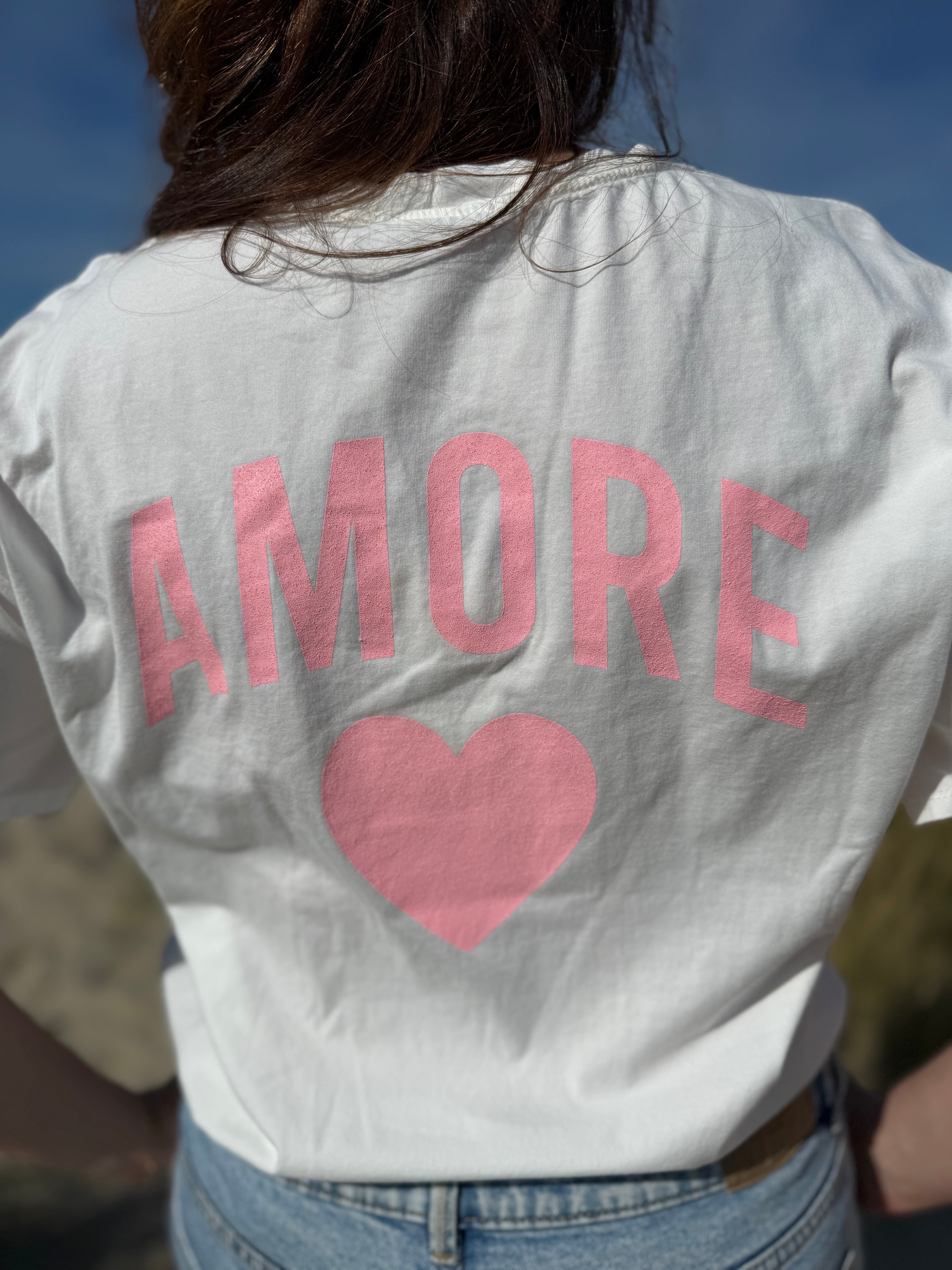 Oversize T-Shirt zum Verlieben. Kleines süßes Herz auf der Brust und ein großer Statement Print auf dem Rücken in rosa mit Amore. Das T-Shirt ist weiß.