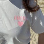 Oversize T-Shirt zum Verlieben. Kleines süßes Herz auf der Brust und ein großer Statement Print auf dem Rücken in rosa mit Amore. Das T-Shirt ist weiß.